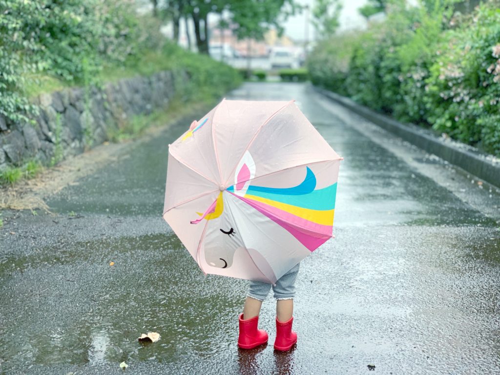 雨の中、長靴を履いて傘をさす小さな女の子