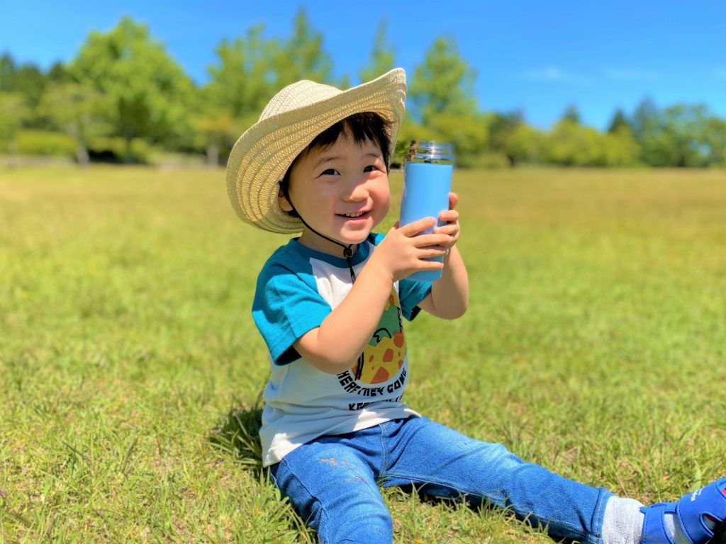 草原で座って水分補給をしようとしている保育園児の男の子